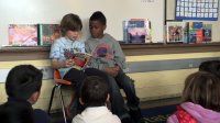 Two primary students are reading in front of the classroom