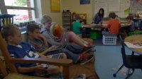 Students in a classroom with teacher working with another group of students in the corner.