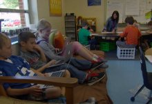 Students in a classroom with teacher working with another group of students in the corner.