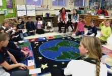 Students and teachers sitting on the classroom floor talking to each other.