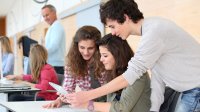 Three teenage students are talking and smiling as they look at a computer tablet.