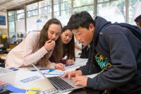 Three middle school students lean over a laptop while working on a class project.