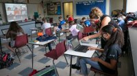 Middle school teacher helps a student at her desk in a hybrid classroom