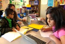 Teacher working with young students on laptops