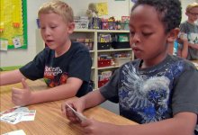 Two boys at a table looking at cards printed with various items to determine want versus need