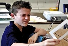 Boy squinting, holding and looking through a cutout in a cardboard frame