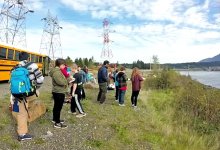 A class off the school bus next to the river taking notes