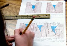 Close up of a hand holding a pencil captioning drawings of water seeping between rocks, freezing and melting