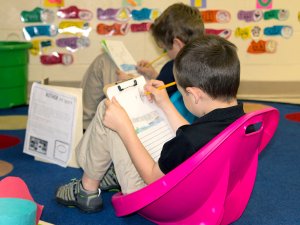 Two young boys writing on clipboards in small rocking chairs