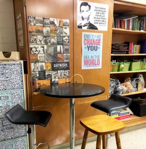 A standing table with stools against a classroom wall