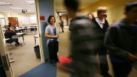 A high school teacher greets students as they enter her classroom