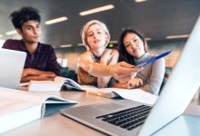 Three students discuss information they’re reading on a laptop.