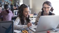 Two girls look at a laptop screen together in class.