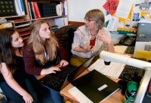 two high school aged students working with a teacher around a computer