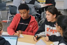 A diverse group of four high school students collaborate at a table at Dayton STEM school