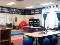 A large, studentless classroom, with large blue bouncy balls, sofa chairs, folding chairs, a tent, crates, mats, and other unique furniture. 