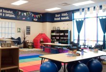 A large, studentless classroom, with large blue bouncy balls, sofa chairs, folding chairs, a tent, crates, mats, and other unique furniture. 