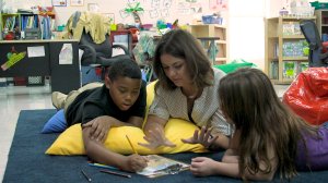 A teacher lying on the floor and helping two students with an assignment at Fall Hamilton Elementary School. 