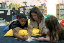 A teacher lying on the floor and helping two students with an assignment at Fall Hamilton Elementary School. 