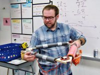 Teacher standing by a whiteboard explaining parts of the base of a weather balloon