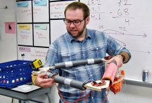 Teacher standing by a whiteboard explaining parts of the base of a weather balloon