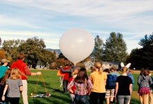 A classroom of kids and teacher out on the field getting ready to release a weather balloon