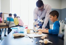 teacher helping hispanic student with science project