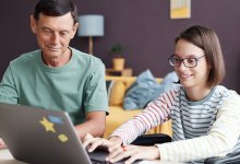 Adult sitting next to a teenager typing on a laptop