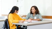 Teacher and student talking while sitting at a desk