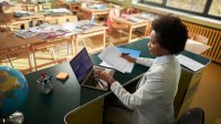 Teacher working on a laptop at her desk in an empty classroom