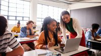 Teacher helps students in class with laptops