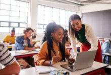 Teacher helps students in class with laptops