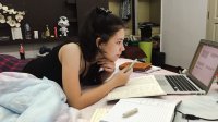 A student studying on her bed with a laptop, textbooks, and notebooks