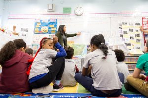 Second graders sit on the floor with a WHEELS alum.