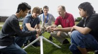 Four boys with an adult on the football field crouched around a rocket