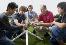 Four boys with an adult on the football field crouched around a rocket