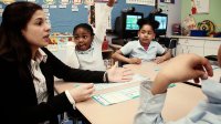 Teacher and three young students sitting together at two desks pushed together in conversation