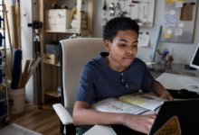 African American teenage boy studying with a textbook is in front of him.