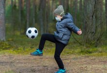 Boy kicking a soccer ball outside while wearing a mask