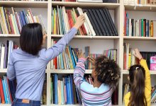 Teacher helps student reach library book off a high shelf