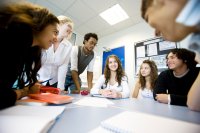 A group of high school students gathered at a table in a circle, doing a language game together