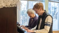 Photo of high school student and elderly woman playing piano