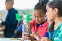 Two students creating a windmill out of a water bottle in science class