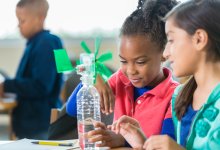 Two students creating a windmill out of a water bottle in science class