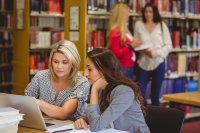 Two teachers working together on a laptop in a school library