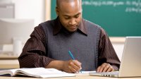 A teacher marks student writing at his desk.