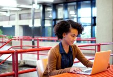 Girl sitting at a table next to stairs working on her laptop