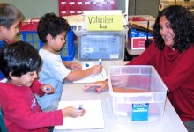 Teacher sitting at a table working with three young boys using markers