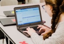 A student works on a coding project on her laptop in a classroom