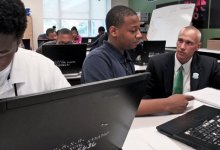 Man crouched down talking to a student who is sitting at his desk